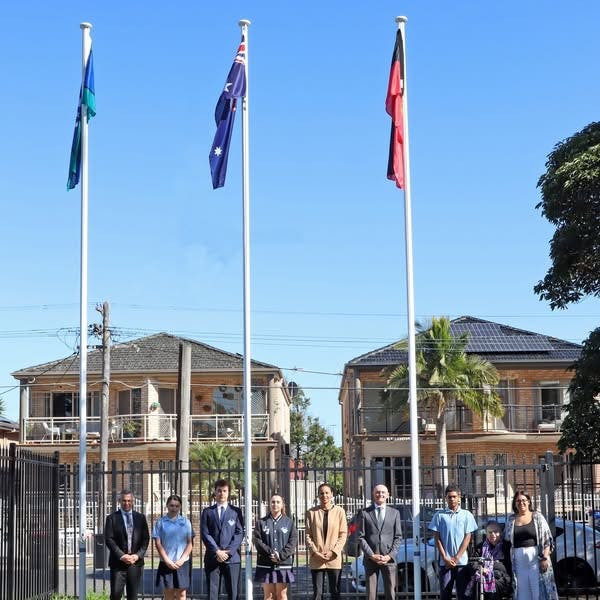 JJ Staff, students and visitor standing in front of 3 flag poles