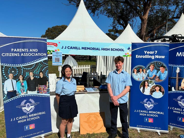 2 students wearing blue uniform standing in front of white tent to promote JJCMHS